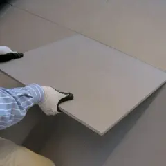 Mani guantate posizionano una piastrella su un pavimento in fase di posa.