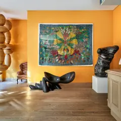 Un soggiorno vibrante con pareti arancioni che esaltano gli effetti pittura pareti moderne. Sculture audaci e un arazzo colorato creano un'atmosfera artistica.