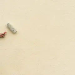 Mano con rullo per pittura facciata esterna, su scala, che rinnova il muro di colore giallo chiaro.