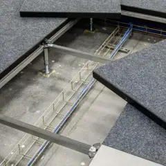 Dettaglio del pavimento galleggiante per ufficio con pannelli grigi in moquette e un'area aperta che rivela cavi e struttura metallica sottostante.