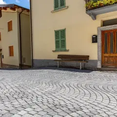 Pavimentazione in pietra per esterni carrabili, con case color pastello e un panchina.