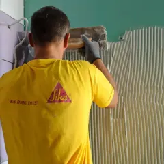 Operaio con maglia gialla Sika applica colla per la partenza posa piastrelle a muro.