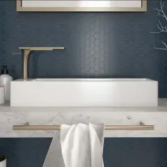 Un elegante bagno con un lavabo rettangolare bianco su un piano in marmo. Le pareti sono rivestite con un bellissimo posa mosaico esagonale blu scuro.
