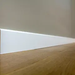 Battiscopa bianco moderno, con un'altezza che definisce lo spazio. Il legno del pavimento riflette la luce.
