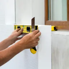 Mani che posano tasselli per cappotto, usando livella e taglierino. Si calcolano quanti tasselli per cappotto al mq per un isolamento perfetto.