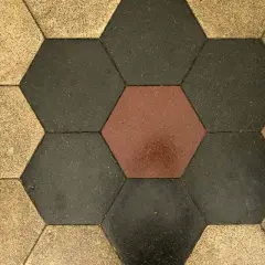 Pavimentazione a nido d'ape con cementine esagonali color ocra, grigio scuro e un tocco di rosso.