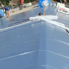 Lavoratori installano un freno vapore su un tetto in costruzione, con rotoli di materiale isolante in primo piano.