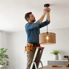 Uomo su scala effettua il montaggio lampadario a sospensione in legno. Attrezzi a portata di mano per un lavoro perfetto.