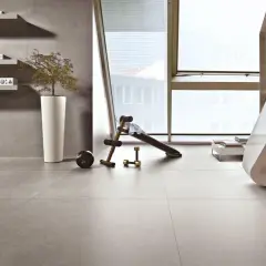 Pavimenti in kerlite per esterni, un angolo fitness con panca e pesi, scaffali con libri e una pianta in vaso.