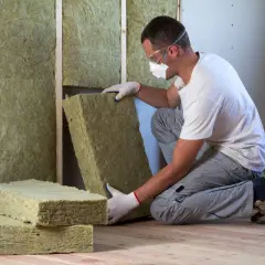 Operaio con maschera e occhiali installa pannelli di cappotto interno lana di roccia per isolare una parete.