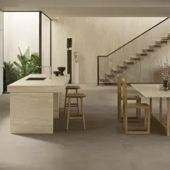 Cucina moderna con isola in travertino e tavolo in legno. Il pavimento non rettificato crea un effetto materico e continuo, integrandosi con le pareti in pietra.