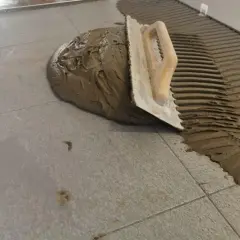 Cazzuola stende cemento per incollare piastrelle grigie. Lavoro in corso.