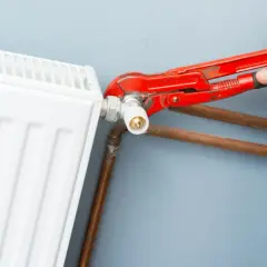 Un idraulico usa una chiave per regolare il raccordo di un termosifone bianco, mostrando come si misura interasse termosifoni per un'installazione corretta.