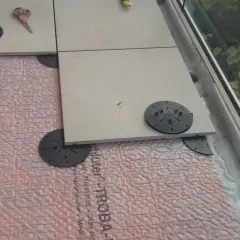 Installazione di un pavimento galleggiante su guaina bituminosa, con piastrelle in fase di posa su supporti regolabili.