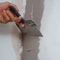 Mano usa una spatola per applicare materiale per chiudere buchi nel muro.