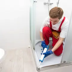 Installatore usa silicone per box doccia, sigillando la base per prevenire perdite d'acqua.