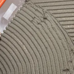 Una spatola dentata stende la colla per piastrelle su una superficie, creando righe uniformi per una posa perfetta.