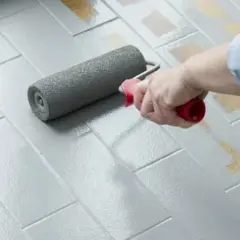 Applicazione di smalto per pavimenti: pro e contro di un restyling fai-da-te. Un rullo grigio stende uniformemente la vernice su piastrelle grigie.