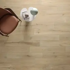 Un tavolino bianco con libro e lampada, accanto a una poltrona marrone, su un pavimento in legno con schemi posa a correre sfalsata.