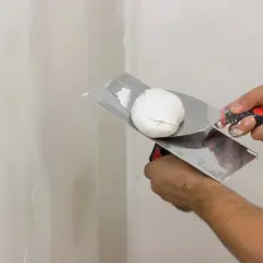 Mani esperte pronte a stuccare muro con spatola e stucco bianco.