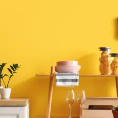 Cucina con pareti giallo vivace, dove **vernici naturali** esaltano gli arredi: piante, pasta in barattoli, piatti rosa e un tagliere in legno.