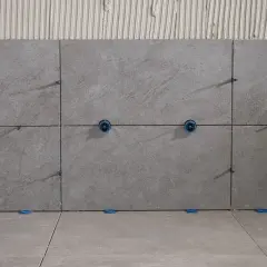 Posa di piastrelle grigie con distanziatori blu. Le fughe piastrelle non rettificate sono visibili, con adesivo sottostante.