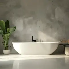 Bagno moderno con vasca freestanding, lavabo in pietra e pareti in resina e piastrelle effetto cemento. Pianta verde e luce naturale.