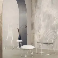 Parete con texture materica e motivi esagonali, che mostra diversi tipi di pittura decorativa. Due sedie bianche minimaliste e tavolini completano l'arredo.