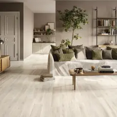 Un soggiorno accogliente con un **pavimento chiaro moderno** che riflette la luce, un divano comodo e una libreria a parete.