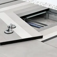 Installazione di un pavimento sopraelevato con pannelli grigi sfumati. Una piastra è sollevata con ventose, rivelando cavi sottostanti.