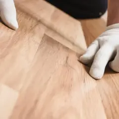 Mani guantate posano un pavimento SPC effetto legno. Valuta il costo posa pavimento SPC per un risultato impeccabile.