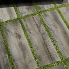 Pavimento posa a secco su erba, con doghe effetto legno grigio alternate a strisce di prato verde. Un tavolino da caffè completa la scena.