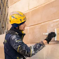 Operaio con casco giallo applica intonaco a un muro, un'alternativa alla rasatura dei muri per un nuovo look.