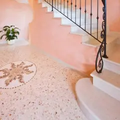 Un elegante pavimento veneziana con un mosaico centrale a forma di sole, accanto a una scala in marmo con ringhiera in ferro battuto.