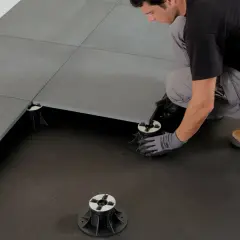 Installazione di un pavimento galleggiante interno con altezza minima. Un operaio posiziona le piastrelle su supporti regolabili.