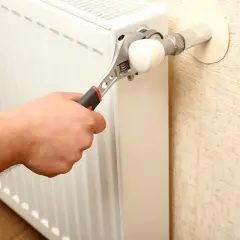 Mano con chiave inglese che regola un termosifone. L'aria nei termosifoni è un problema comune.