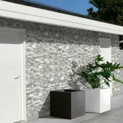 Muro esterno con rivestimento in pietra, che mostra diversi tipi di mattoni per muri esterni. Due porte bianche e fioriere moderne completano la scena.