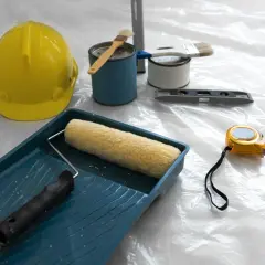Attrezzi da lavoro: casco giallo, rullo, pennelli, livella, metro e barattoli di vernice, pronti per applicare l'intonaco per umidità.