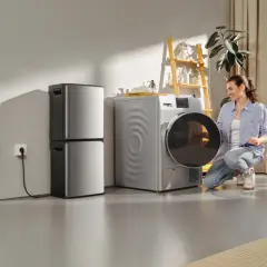 Donna sorride vicino a una lavatrice e asciugatrice, parte di soluzioni per il risparmio energetico. Cesto di biancheria accanto.