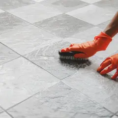 Mani con guanti arancioni puliscono piastrelle molto sporche con una spazzola e schiuma.