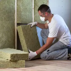 Operaio con maschera e occhiali installa pannelli isolanti per un cappotto interno.