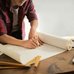 Un uomo disegna su un rotolo di carta, pianificando la posa di piastrelle al metro quadro.