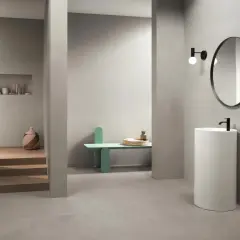 Bagno moderno con rivestimento uguale al pavimento, lavabo a colonna, specchio rotondo e nicchia con oggetti decorativi.