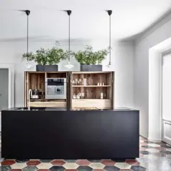 Cucina moderna con isola nera, pensili in legno, piante e pavimento con cementine esagonali colorate.