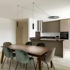 Un lampadario decentrato crea un'atmosfera moderna sopra un tavolo da pranzo in legno con sedie in velluto verde. Soluzioni di illuminazione eleganti per ogni spazio.