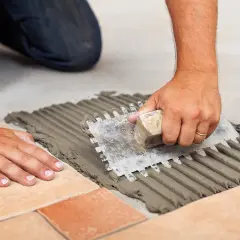 Mani esperte stendono la colla per piastrelle con una spatola dentata, creando un letto uniforme. La quantità di colla per piastrelle al mq è fondamentale per una posa perfetta.