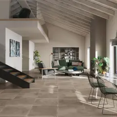 Pavimento con effetto cemento in un soggiorno moderno con scala a vista, divano verde e zona pranzo.
