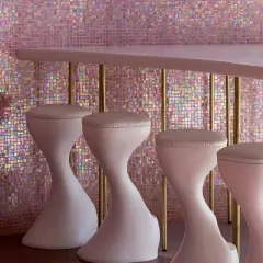 Un bancone rosa pallido con sgabelli bianchi si staglia contro un muro scintillante di **bisazza ceramiche** iridescenti, creando un'atmosfera glamour.