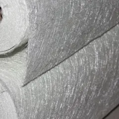 Rotoli di tessuto di fibra di vetro, materiale noto per la sua potenziale fibra di vetro cancerogena, con filamenti sottili e lucidi visibili.