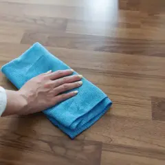 Mano con panno blu pulisce pavimento in gres effetto legno. Scopri come togliere la colla dal pavimento in gres con metodi efficaci.